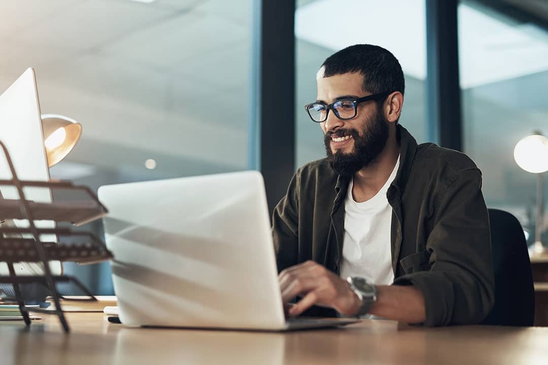 A young businessman happily communicating in the office using a laptop.
